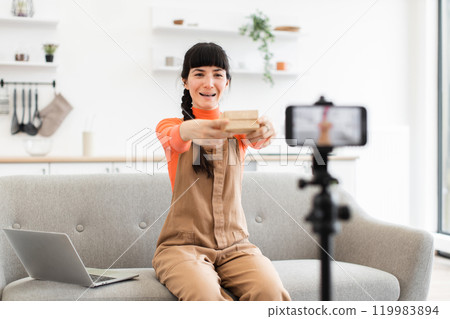 Caucasian female blogger unboxing gift while recording video at home Caucasian female blogger unboxing gift while recording video at home 119983894