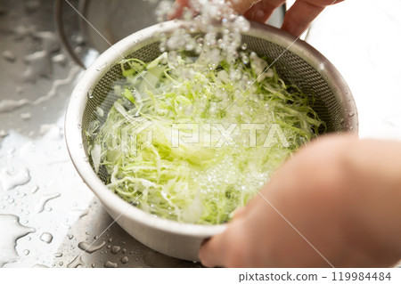 A middle-aged to senior woman washing shredded cabbage in her kitchen 119984484