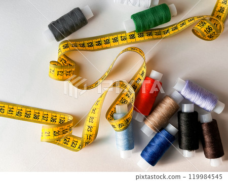 Colorful spools of thread and yellow measuring tape for sewing crafts 119984545
