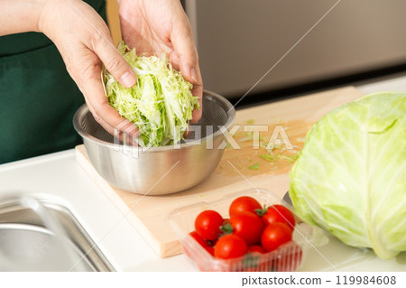 A middle-aged to senior woman washing shredded cabbage in her kitchen 119984608