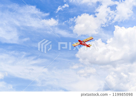 Red single-engine ultralight airplane flying in the blue sky with white clouds 119985098