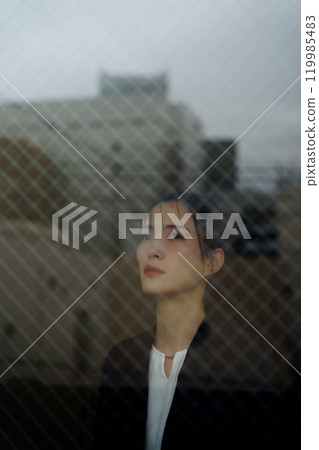 A young woman in a suit with a melancholy expression and a cityscape reflected through the glass 119985483