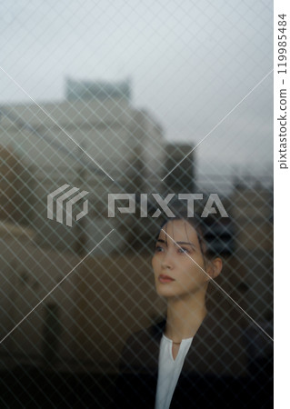 A young woman in a suit with a melancholy expression and a cityscape reflected through the glass 119985484