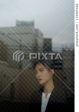 A young woman in a suit with a melancholy expression and a cityscape reflected through the glass A young woman in a suit with a melancholy expression and a cityscape reflected through the glass 119985488