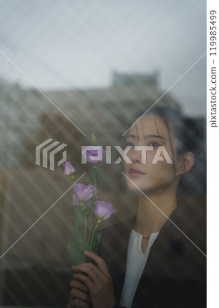 一位穿著西裝的年輕女子，表情憂鬱，透過玻璃倒映著城市景觀 119985499