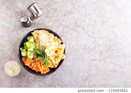 Thin pancakes or crepes with smoked salmon, cucumber and dill on a gray background. Thin pancakes or crepes with smoked salmon, cucumber and dill on a gray background. 119985662