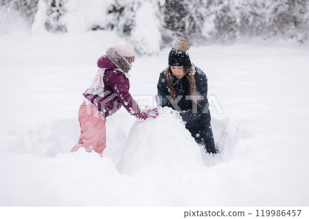 Mother and daughter enjoy a snowy day together, creating memories and sharing winter joy in a beautiful landscape 119986457
