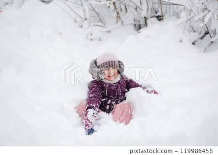 A little girl in winter clothing smiles joyfully while surrounded by deep snow, capturing the magic of a snowy winter day 119986458