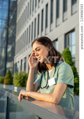 Young female doctor standing near clinic and feeling tired Young female doctor standing near clinic and feeling tired 119986583