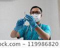 Healthcare Worker Inspecting Syringe Before Injection with Protective Gear 119986820