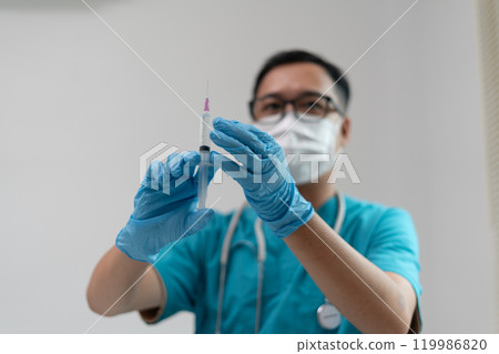 Healthcare Worker Inspecting Syringe Before Injection with Protective Gear 119986820