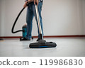 Person Vacuuming Floor with Modern Vacuum Cleaner in Minimalist Room 119986830