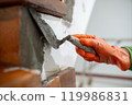 A person is using a trowel to apply cement to a wall. 119986831