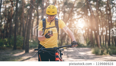 Cyclist checking route on smartphone during ride in forest Cyclist checking route on smartphone during ride in forest 119986928