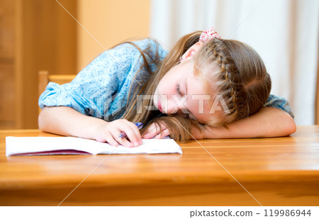 Small girl sleeping on a desk in a classroom 119986944
