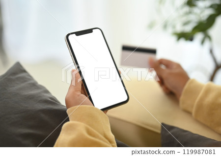 Close up woman making an online purchase with credit card and smartphone 119987081