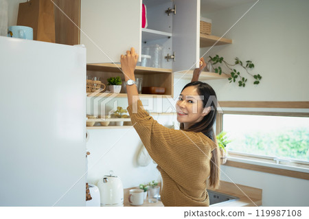 Smiling young woman organizing kitchen cabinet in cozy home 119987108