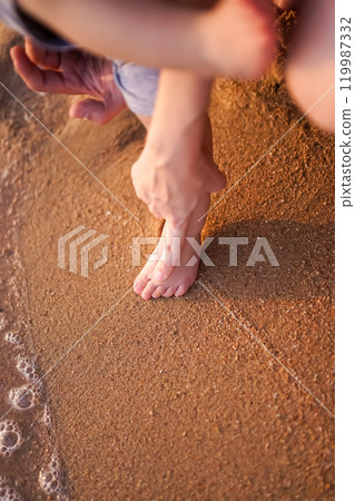 The joyful picture of the baby first step footprint on the glittering sand at the beach with the parents filled with love and kindness. The air bubble of the seawater. Mother hand on child foot 119987332