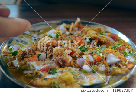 A vibrant plate of bhel puri chaat garnished with sev, onions, tomatoes, and herbs which is a local authentic street food originating from Mumbai, India 119987397