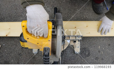 Man in glove holds board with one hand and saws it with hand-held circular saw, top view, cutting board on miter saw Man in glove holds board with one hand and saws it with hand-held circular saw, top view, cutting board on miter saw 119988193