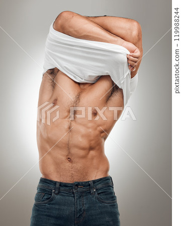 Man, tshirt and take off in studio for fitness, wellness and strong abs muscle on gray background. Male person, clothes and undressing for health, bodybuilder and proud of body or workout results 119988244