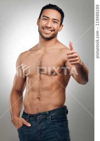 Thumbs up, fitness and Asian man in portrait with smile, body positivity and topless in studio. Happy person, approval and proud of progress from exercise, wellness and goal on gray background 119988288