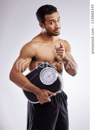 Pointing, portrait and man with scale for fitness in studio for body care, wellness and diet for muscles. Male person, athlete or bodybuilder and smile for weight loss or exercise by white background 119988345