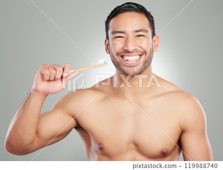 Portrait, happy man and brushing teeth in studio for dental hygiene, wellness or oral health. Face, toothpaste or cleaning with natural bamboo toothbrush for orthodontics isolated on gray background 119988740