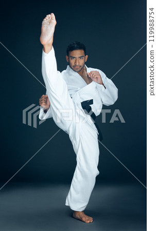 Karate, training and portrait of man kick in studio for practice, exercise or fitness. Serious, fight and male person with martial arts skill for self defense technique isolated by black background. 119988754