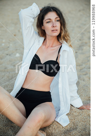 Portrait of a beautiful woman in a black swimsuit on the beach by the sea Portrait of a beautiful woman in a black swimsuit on the beach by the sea 119988968