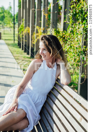 woman in light summer dress smiling in park on walk 119988975