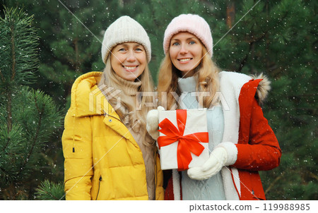 Happy smiling women friends, gift box, celebration on Christmas tree background in winter forest Happy smiling women friends, gift box, celebration on Christmas tree background in winter forest 119988985