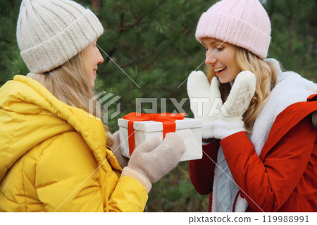 Happy smiling women friends, gift box, celebration on Christmas tree background in winter forest Happy smiling women friends, gift box, celebration on Christmas tree background in winter forest 119988991