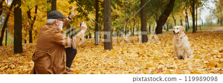 Elderly man in coat strolling through autumn park, his golden retriever happily playing, executes owner's commands Elderly man in coat strolling through autumn park, his golden retriever happily playing, executes owner's commands 119989098