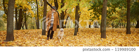Banner. Elderly man and his retriever explore park, where fallen yellow and orange leaves create, vibrant backdrop. 119989100