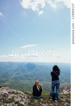 Two female traveler looking at the view from the top of the mountain on a hike 119989137