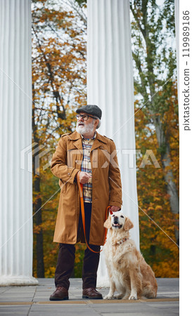 Happy dog and elderly owner, man dressed vintage outfit enjoy calm walk together through park filled with vibrant autumn colors. Happy dog and elderly owner, man dressed vintage outfit enjoy calm walk together through park filled with vibrant autumn colors. 119989186