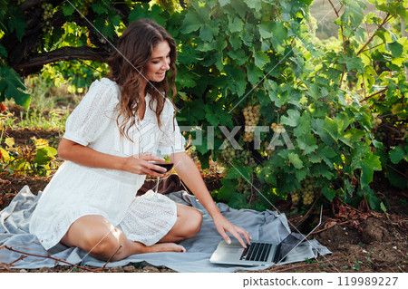 Woman working online on laptop in vineyard with wine Woman working online on laptop in vineyard with wine 119989227