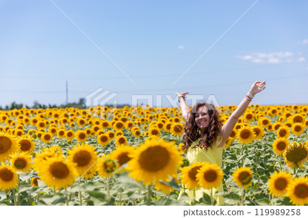 Red-haired woman in yellow dress in sunflower field smiling 119989258