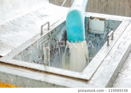Milky white liquid gush out of the blue plastic industrial water pipe and flow through metal filter. Milky white liquid gush out of the blue plastic industrial water pipe and flow through metal filter. 119989336