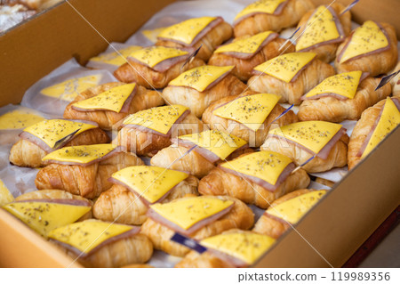Appetizing croissant ham and cheese sandwiches in a paper box, enhanced with oregano spray. 119989356