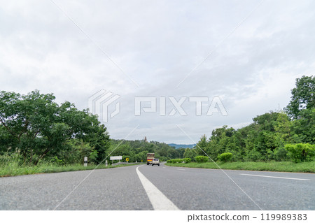 A ground-level perspective of a rural street in Tak Province, Thailand, in open sky during the day. This road serves as key transportation artery to western region of country. 119989383