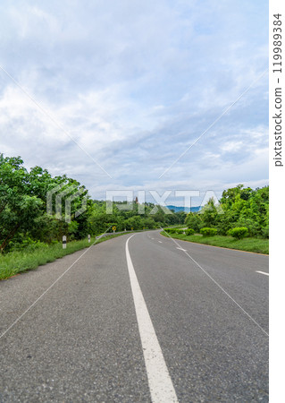 A ground-level perspective of a rural street in Tak Province, Thailand, in open sky during the day. This road serves as key transportation artery to western region of country. 119989384