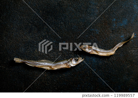Two dried sun-dried sea fish smelt hamsa anchovy on dark textured background. Salty traditional appetizer. Sea food background 119989557