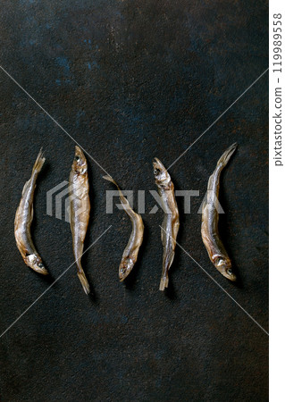 Heap dried sun-dried sea fish smelt hamsa anchovy in row on dark textured background. Salty traditional appetizer. Sea food background 119989558