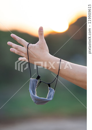 Close up to textile fabric mask is hanged on to man arm with the twilight background. 119989615