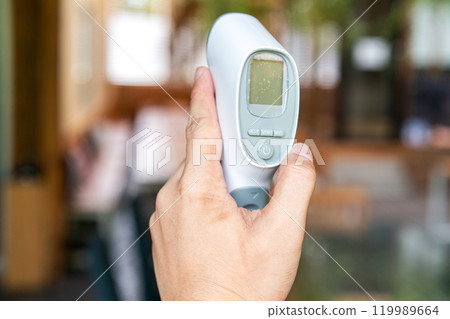Thermometer Gun in Man Hand. It Digital Infrared Sight Temperature Measurement Device on wood table in outdoor field. Clipping Path. 119989664