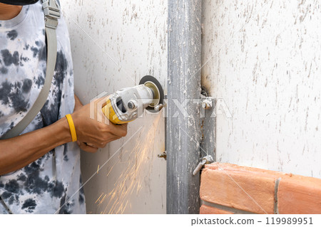 Asian worker young man sawing and kept detailed metal screw from a steel pole for preparing to install foam brick wall. 119989951