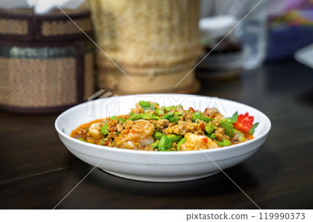 Thai Stir-Fried Stink Beans with Shrimps and spicy shrimp paste sauce in white dish bowl on dark wood table. 119990373