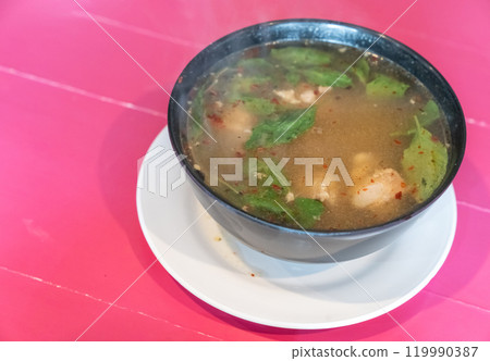 Traditional thai spicy Tom yum soup with chicken served in black bowl and on white dish with wooden pink table 119990387